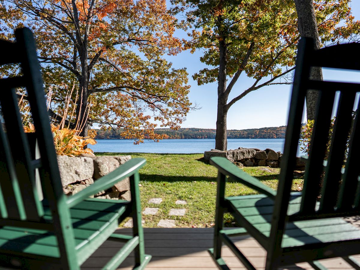 Green deck chairs frame an autumn lakeside view with colorful trees, green grass, and a calm blue lake.