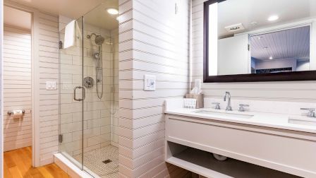A modern bathroom with a glass-enclosed shower, white tile walls, and a double sink vanity with a large mirror.