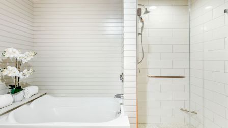 A modern bathroom with a white bathtub on the left and a glass-enclosed shower on the right, both featuring white subway tiles and clean lines.
