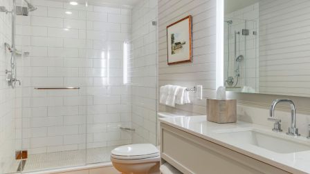 A modern bathroom with a glass-walled shower, white subway tile, a double-sink vanity, a wall mirror, and wooden floor.