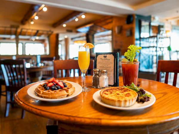 Brunch on a wooden table&mdash;waffle and pastry, fresh juice cocktails, flowers, and a cozy caf&eacute; interior around.