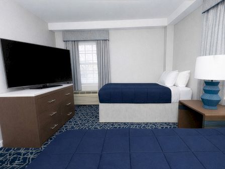 A tidy hotel room with two queen beds, a dresser with a flat-screen TV, a nightstand, and a blue-accent decor scheme.
