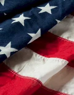 A close-up of an American flag showing blue stars and bold red-and-white stripes, waving in the light.