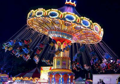 A bright nighttime carnival ride with colorful lights and a crowd gathered in front of it.