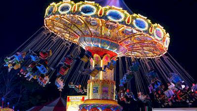 A bright nighttime carnival ride with colorful lights and a crowd gathered in front of it.