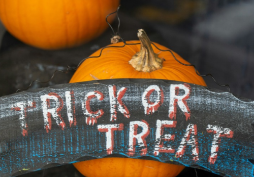 Pumpkins with a weathered Halloween sign reading &ldquo;RICK OR TREAT,&rdquo; plus a small jack-o&rsquo;-lantern-style decoration behind it.