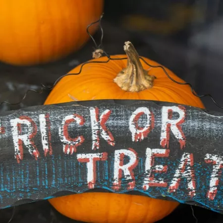Pumpkins with a weathered Halloween sign reading &ldquo;RICK OR TREAT,&rdquo; plus a small jack-o&rsquo;-lantern-style decoration behind it.