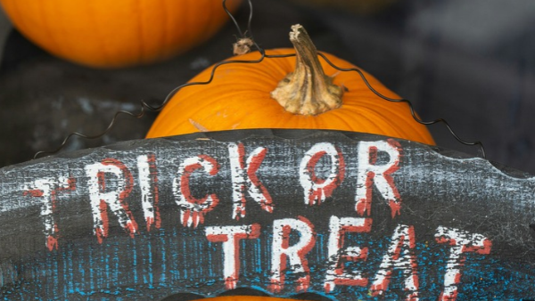 Pumpkins with a weathered Halloween sign reading &ldquo;RICK OR TREAT,&rdquo; plus a small jack-o&rsquo;-lantern-style decoration behind it.
