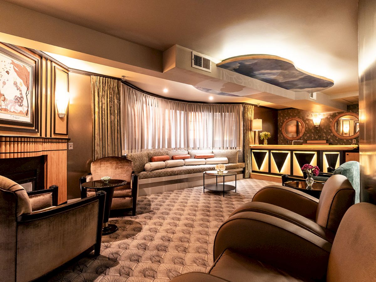 A cozy lounge with plush seating, a fireplace, soft lighting, art on walls, curtained windows, and a bar-like cabinet along the back.