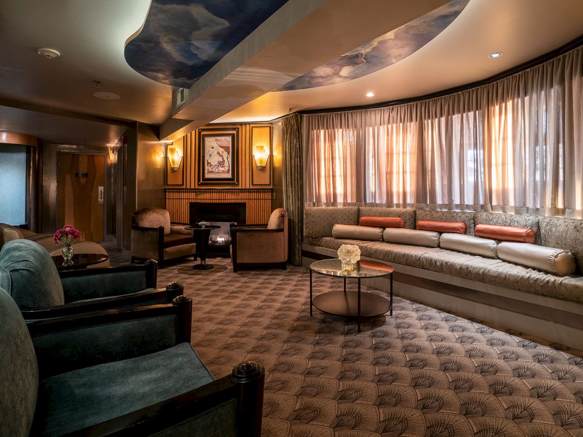 A luxurious lounge with curved sofa seating, plush chairs, warm lighting, ceiling sky mural, and a carpeted floor; calm, upscale vibe.