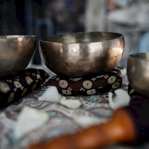 Three metal singing bowls on a patterned cloth, with a blurred hand nearby, likely a Tibetan tea or meditation setup.