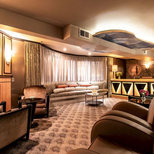 A luxurious lounge with plush seating, warm lighting, a fireplace, and a long sofa by windows; upscale bar area on the right.