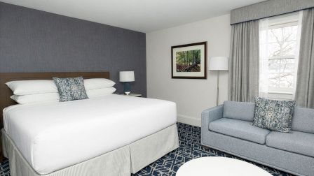 A hotel room with a king bed, two nightstands, blue accent wall, a sofa, coffee table, and a window with curtains.