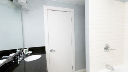 A modern bathroom with a white door, black countertop sink, and a white-tiled shower area featuring a silver faucet and shower head.