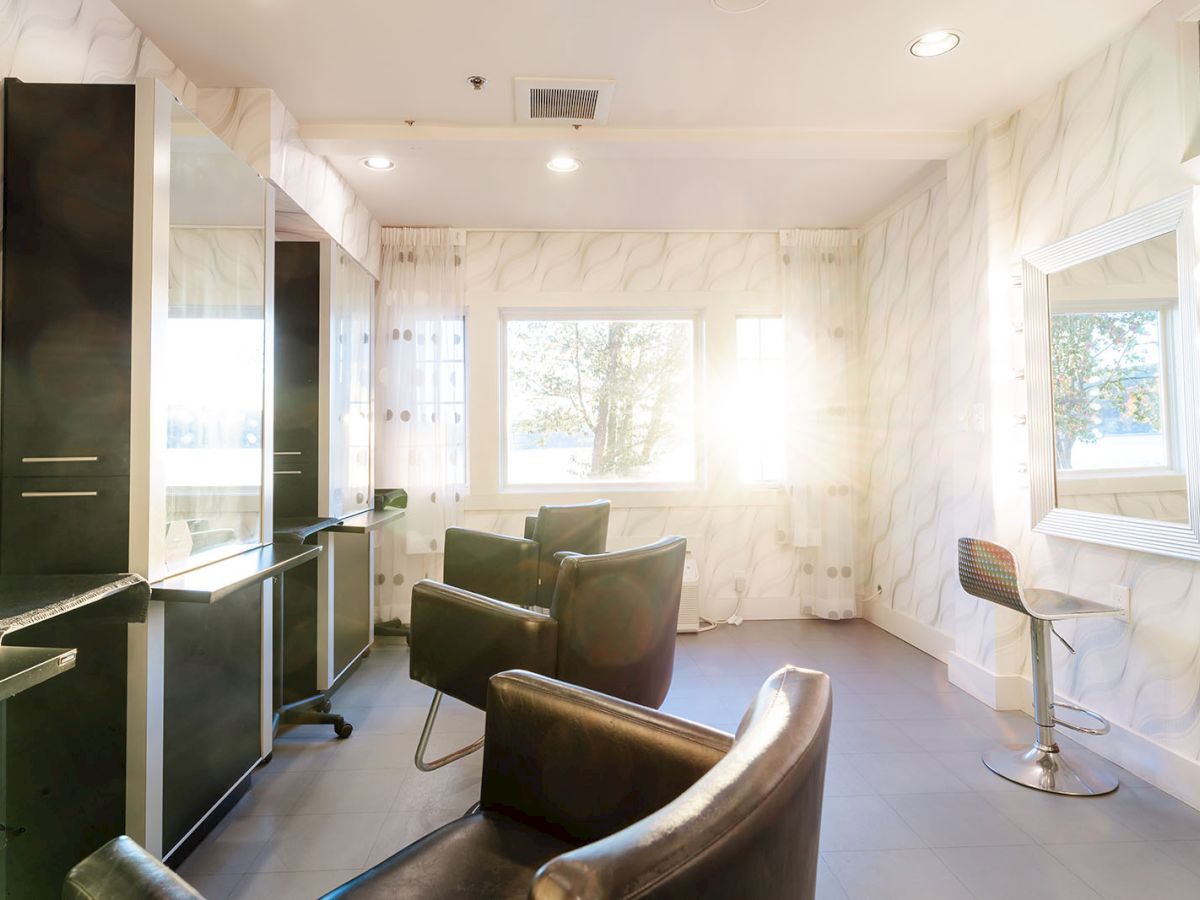 A modern, bright hair salon with black styling chairs, mirrors, and white marble walls, plus a windowed back room and tidy stations.