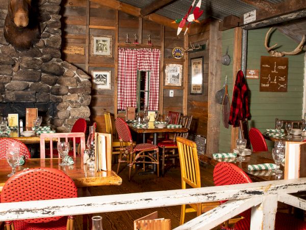 The image shows a cozy, rustic restaurant interior with wooden walls, red checkered tablecloths, framed pictures, and various decorative items.