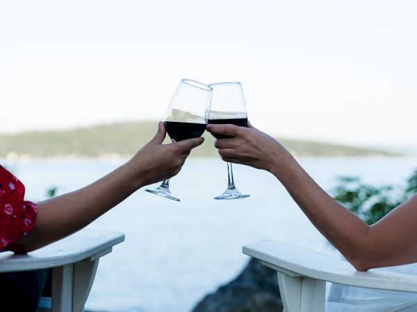 Two people clinking wine glasses on a scenic seaside balcony, enjoying a sunset toast.