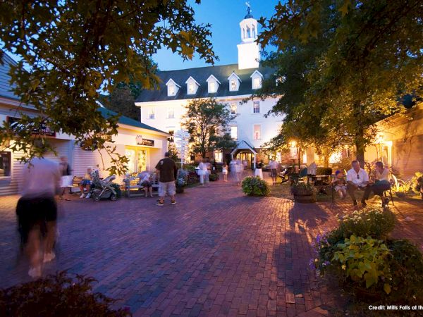 A charming courtyard scene with people strolling and sitting, surrounded by historic buildings under evening light. Ends the sentence.