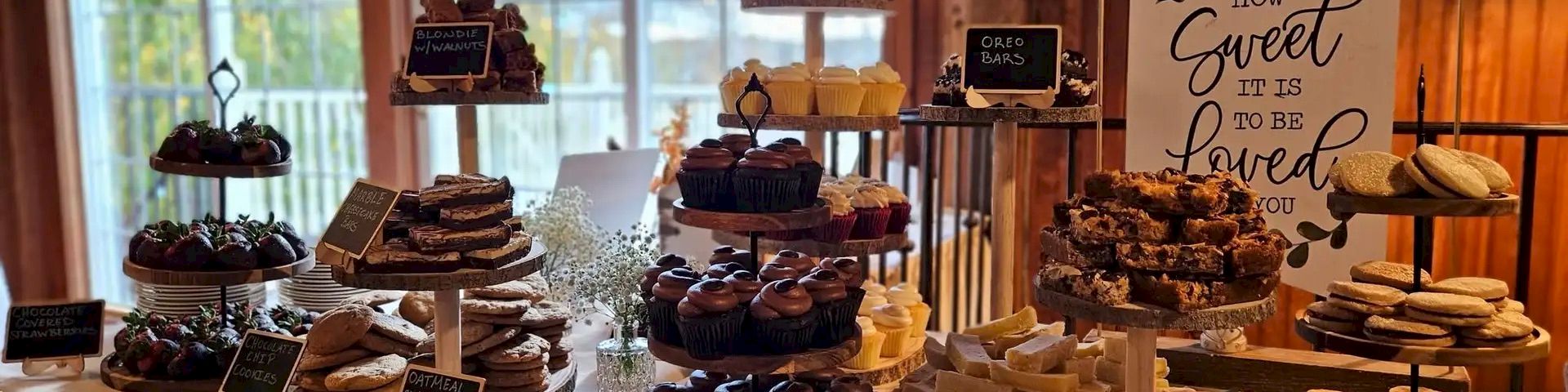 A cozy cake table with multiple stacked stands of desserts, chalkboard signs, soft lighting, and a &ldquo;You are loved&rdquo; printable sign in the background.