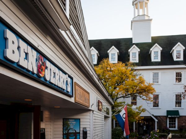 A building with a "Ben & Jerry's" sign, a tree with yellow leaves, and a large white colonial-style building in the background.
