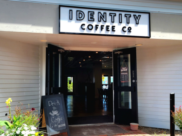 Entrance of Identity Coffee Co. with an open door, a chalkboard sign advertising drinks, and surrounding plants.