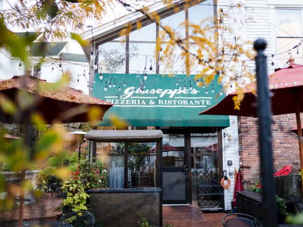 The image shows the entrance to Giuseppe's Pizzeria & Ristorante, surrounded by outdoor seating and greenery, with string lights above the patio area.