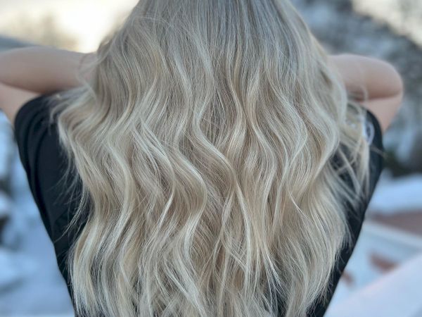 A person standing outside with their back to the camera, displaying long, wavy blonde hair. The setting appears to be outdoors in a snowy area.