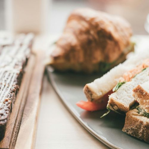 A plate with a tri-tip sandwich or crusty bread slices and a pastry in the background, set on a cafe-style breakfast table.