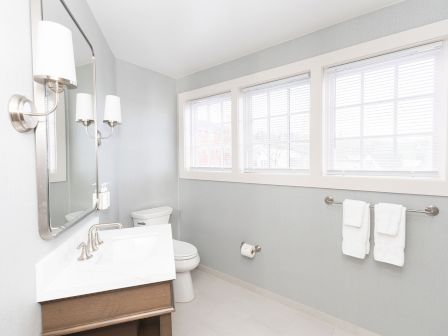 A modern bathroom with a double vanity, wall-mounted mirror lights, a toilet, and a large window with towel bars and neatly folded towels.