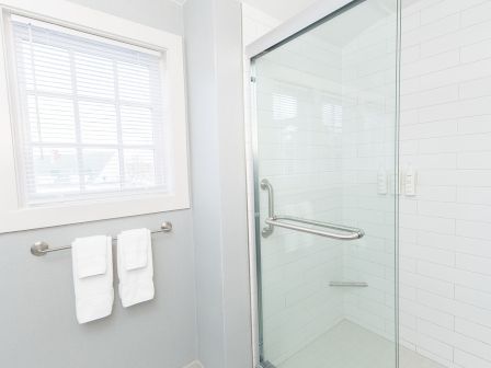 A modern bathroom with a glass shower enclosure, white subway tile, a towel rack with two white towels, and a window with blinds, bright and clean.