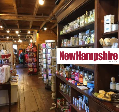 This image shows a cozy store with wooden floors, shelves stocked with various products, and a "New Hampshire" magazine sign prominently displayed.