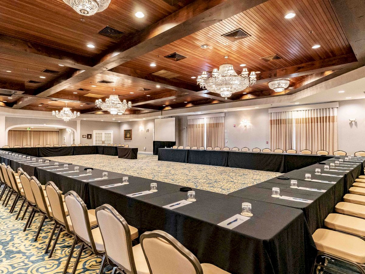 A banquet hall with a large U-shaped table setup, chairs, and chandeliers, ready for a formal event or meeting, with elegant decor and lighting.