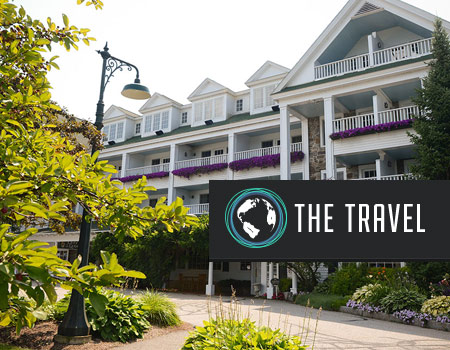 The image features a multi-story building with white railings, lush greenery, and a sign that reads "The Travel" with a globe icon.