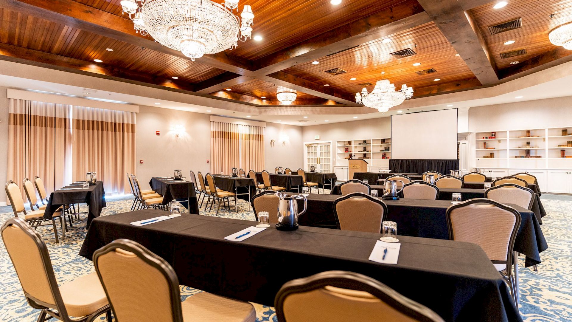 This image shows a conference room setup with tables and chairs, chandeliers, and a projector screen, creating an elegant and professional atmosphere.