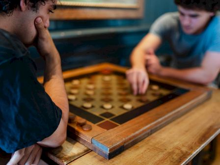 Two people are engrossed in a board game, focusing intently on their moves, indicated by the strategic placement of pieces on the board.