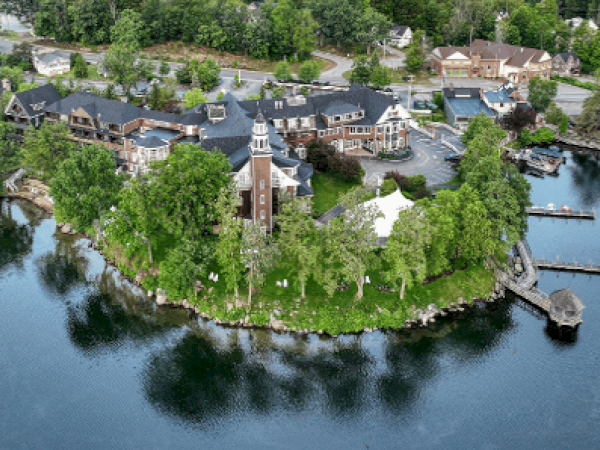 An aerial view of a lakeside estate with a large building, trees, a dock, and surrounding water, likely a resort or institutional facility.