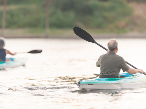 Two people are kayaking on a calm body of water, each in their own kayak. The setting appears tranquil and serene.