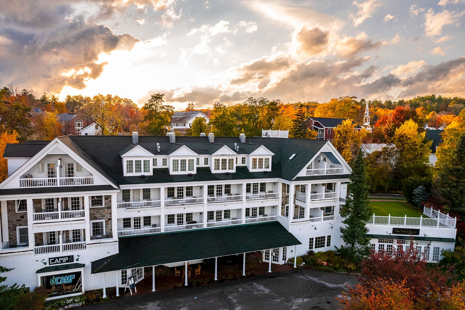 A large white building with a green roof sits amidst colorful autumn foliage under a partly cloudy sky at sunset.