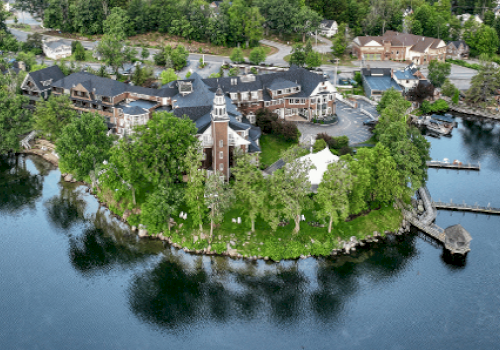 An aerial view of a waterfront property with multiple buildings surrounded by trees and water, featuring docks and a lighthouse-style structure.