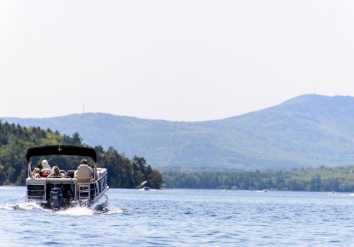 A small motorboat on a lake with people onboard, water, and distant tree-lined hills/mountains under a clear sky. Top it at 140 characters, always ending the sentence.