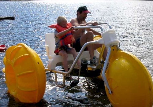 A man and a child are on a yellow water tricycle, pedaling on a lake with life vests on.