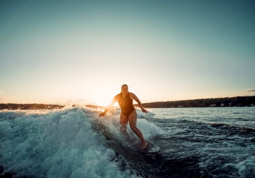 A person is surfing a wave at sunset, gliding along the water with the sun low on the horizon.