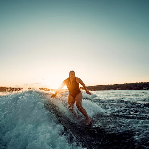 A person is surfing a wave at sunset, gliding along the water with the sun low on the horizon.