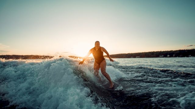 A person is surfing a wave at sunset, gliding along the water with the sun low on the horizon.