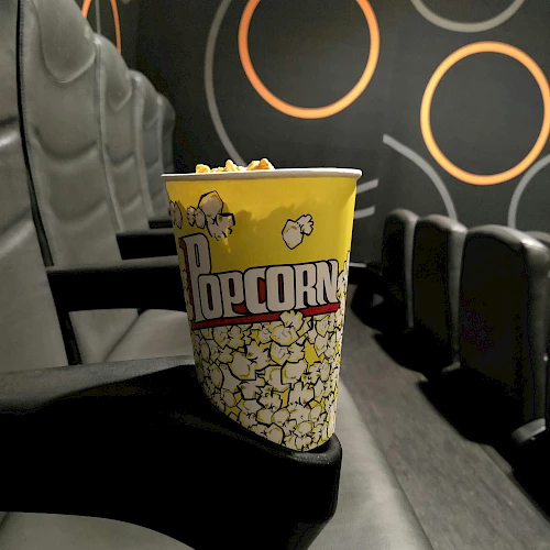 A bucket of popcorn on a theater seat, with a dark, circular pattern wall in the background.