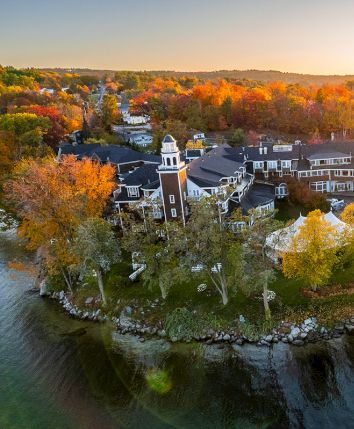 Aerial view of an autumn riverside town with leafy trees, houses, and wooden docks at sunset.
