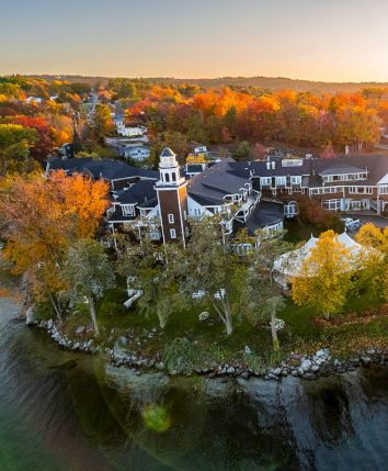 Aerial view of a riverside town in autumn, with colorful trees, houses, and wooden docks catching sunset light.