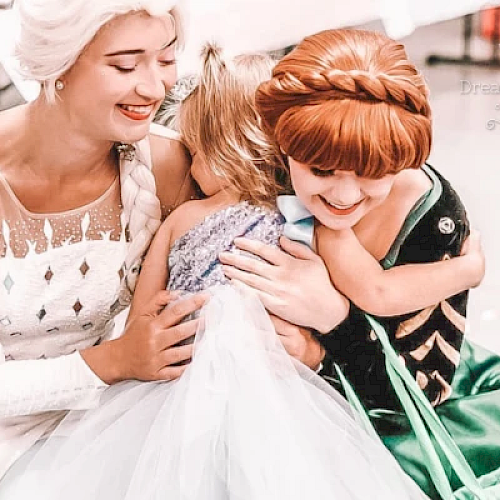 Two women in princess costumes hugging a child dressed as a princess, with joyful expressions.