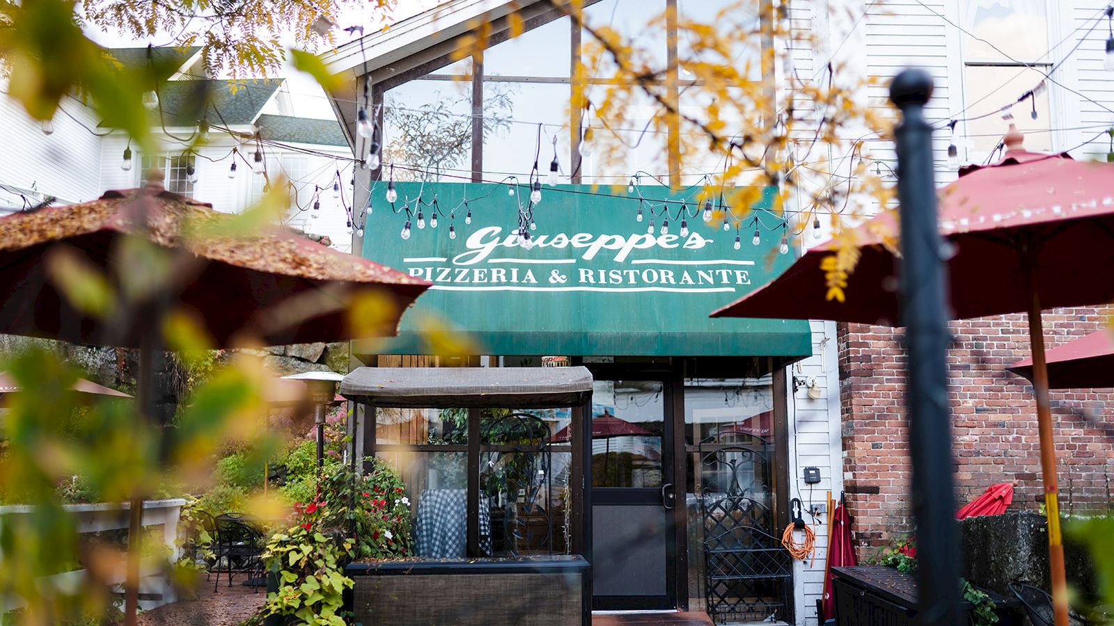 The image shows the entrance of a restaurant with the sign "Giuseppe's Pizzeria & Ristorante," featuring outdoor seating and greenery.