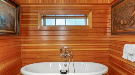 A freestanding bathtub in a wood-paneled bathroom with two framed artworks on the walls and a towel hanging on the right.